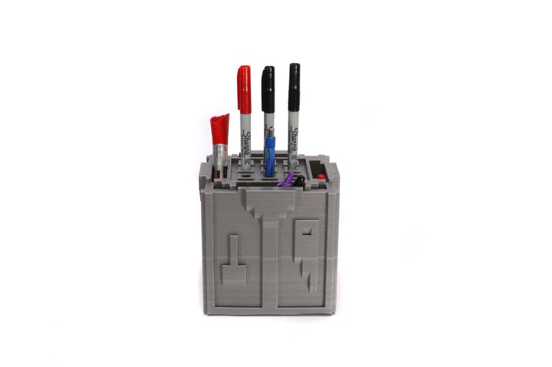May include: Gray 3D printed pen holder with a maze design. The holder has four slots for pens and markers. There are three black Sharpie markers and one red marker in the holder.