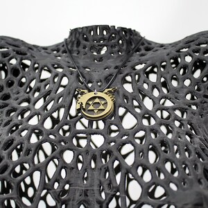 May include: A gold-toned necklace with a pendant featuring a star of David and wings. The necklace is displayed on a black, 3D printed, mesh-like mannequin.