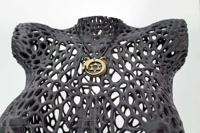 May include: A gold-toned necklace with a pendant featuring a star of David and wings. The necklace is displayed on a black, 3D printed, mesh-like mannequin.