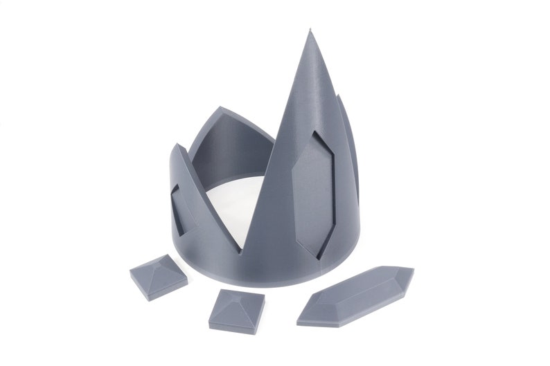 May include: A gray plastic crown with a pointed top and four separate pieces. The crown is designed to be assembled.