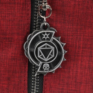 May include: A silver metal zipper pull with a Dungeons and Dragons themed design. The design features a 20-sided die, a skull, and a star.