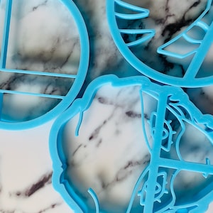 May include: Three blue plastic cookie cutters, one shaped like a circle with a grid pattern, one shaped like a flower with a swirl pattern, and one shaped like a geometric design.
