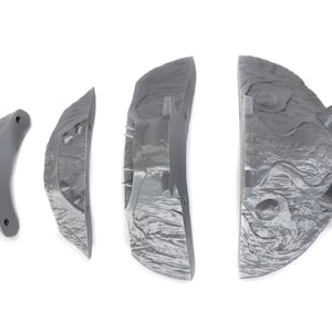 Puede incluir: Cinco piezas grises de una m&aacute;scara de monstruo impresa en 3D. Las piezas son texturizadas y tienen bordes afilados.