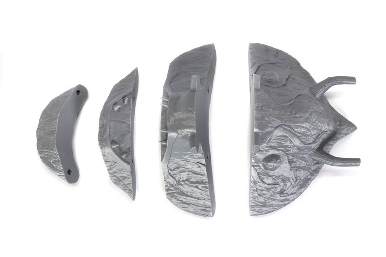 Puede incluir: Cinco piezas grises de una m&aacute;scara de monstruo impresa en 3D. Las piezas son texturizadas y tienen bordes afilados.