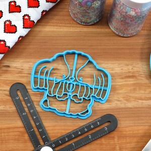 May include: Blue plastic cookie cutter shaped like a cartoon dog wearing a sweater. The cutter is on a wooden surface.
