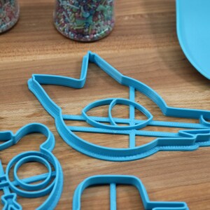 May include: A set of four blue plastic cookie cutters shaped like a wolf, a bear wearing glasses and a hat, a cat, and a microphone.
