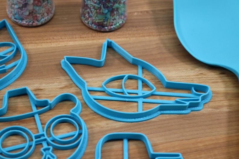 May include: A set of four blue plastic cookie cutters shaped like a wolf, a bear wearing glasses and a hat, a cat, and a microphone.
