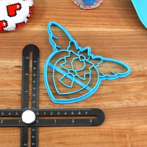 May include: Blue plastic cookie cutter shaped like a heart with wings. The heart has a smaller heart inside of it.