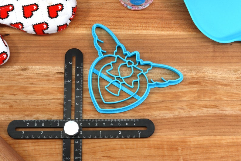 May include: Blue plastic cookie cutter shaped like a heart with wings. The heart has a smaller heart inside of it.