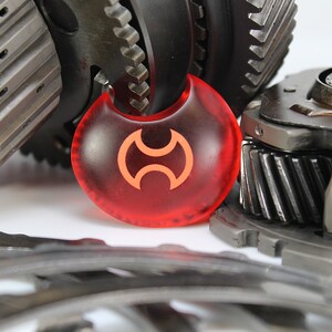 May include: A red, crescent-shaped object with a stylized orange symbol in the center. The object is surrounded by several metal gears.