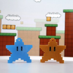 May include: Two pixelated star-shaped keychains, one blue and one gold, against a backdrop of a video game level.