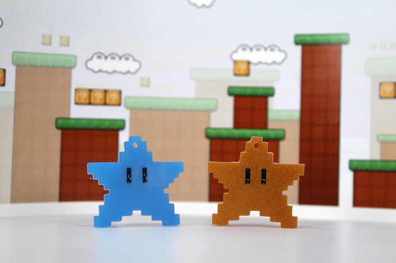 May include: Two pixelated star-shaped keychains, one blue and one gold, against a backdrop of a video game level.