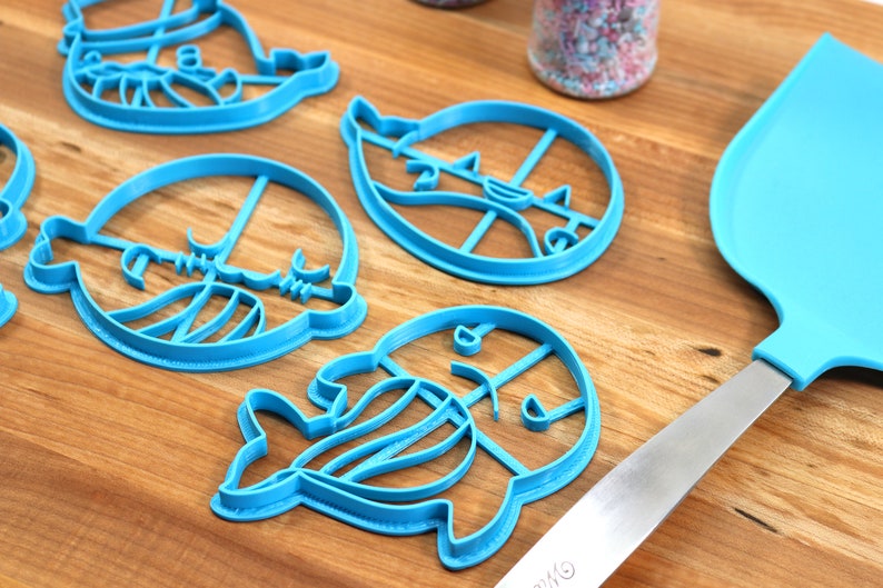 Peut inclure: Un ensemble de cinq emporte-pi&egrave;ces en plastique bleu en forme de cr&eacute;atures marines. Les emporte-pi&egrave;ces sont sur une surface en bois avec une spatule bleue.