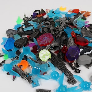 May include: A collection of colorful plastic and metal charms, including swords, stars, rings, and other shapes. The charms are in various colors, including blue, red, green, and orange.
