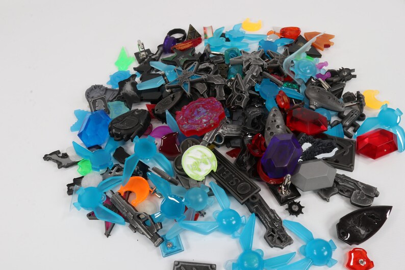 May include: A collection of colorful plastic and metal charms, including swords, stars, rings, and other shapes. The charms are in various colors, including blue, red, green, and orange.