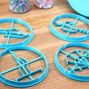May include: Four blue plastic cookie cutters with different designs. The cutters are on a wooden surface.