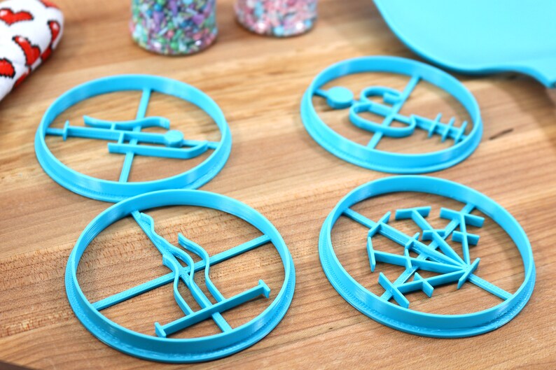 May include: Four blue plastic cookie cutters with different designs. The cutters are on a wooden surface.