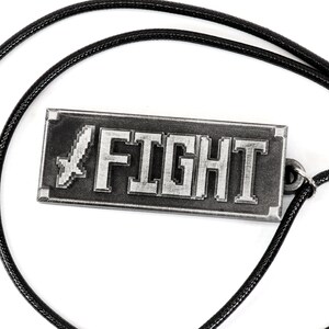 May include: A silver-colored necklace with a rectangular pendant that says "FIGHT" in pixelated letters. A pixelated sword is to the left of the word "FIGHT". The necklace is on a black cord.