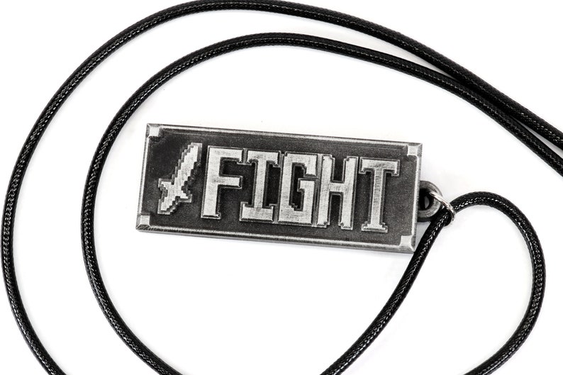 May include: A silver-colored necklace with a rectangular pendant that says "FIGHT" in pixelated letters. A pixelated sword is to the left of the word "FIGHT". The necklace is on a black cord.