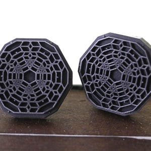 May include: A pair of octagonal cufflinks with a geometric design in a dark gray color.