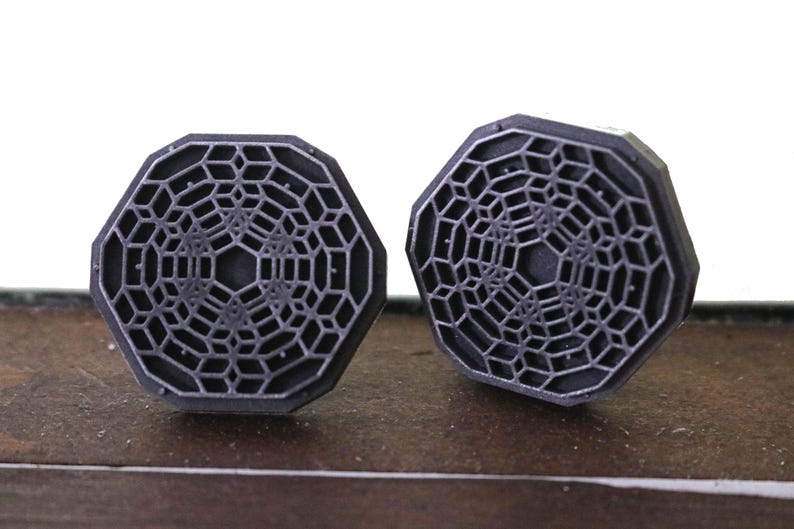 May include: A pair of octagonal cufflinks with a geometric design in a dark gray color.