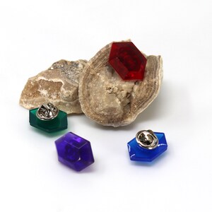 May include: Three hexagonal pins with a silver pin back. The pins are red, green, and blue.