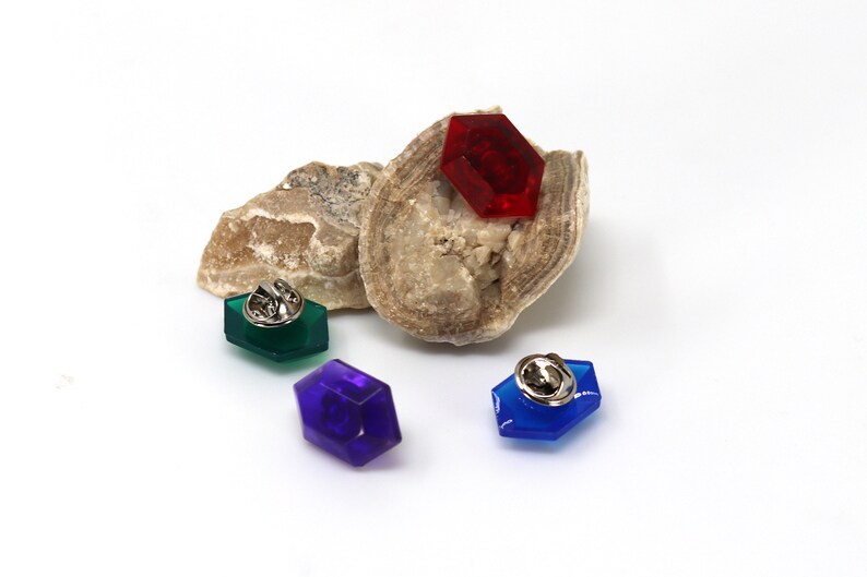 May include: Three hexagonal pins with a silver pin back. The pins are red, green, and blue.