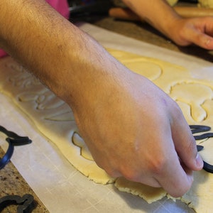 May include: A person using cookie cutters to cut out shapes from a sheet of dough on a white surface.