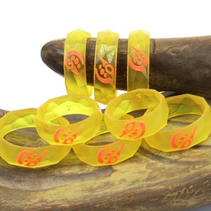 May include: A set of six yellow resin rings with a red design. The rings are stacked on a wooden surface.