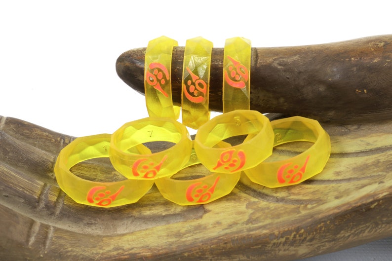 May include: A set of six yellow resin rings with a red design. The rings are stacked on a wooden surface.