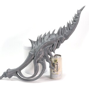 May include: A gray 3D printed sword with a sharp, jagged blade and a curved handle. The sword is resting on a white surface next to a can of Japanese beer.