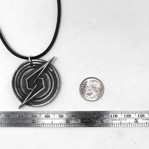 May include: A silver necklace with a pendant featuring a stylized lightning bolt design. The pendant is about 2 inches in diameter and is on a black cord.