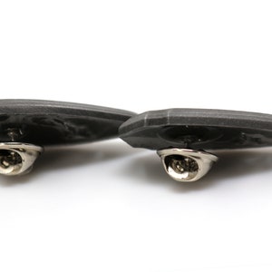 May include: Two gray metal pins with a detailed design. The pins have a silver-colored clasp on the back.