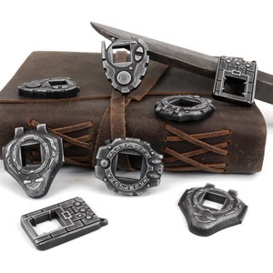 May include: Eight silver-colored metal charms shaped like digital watches with different designs. The charms are arranged on a brown leather-bound journal with a silver knife.