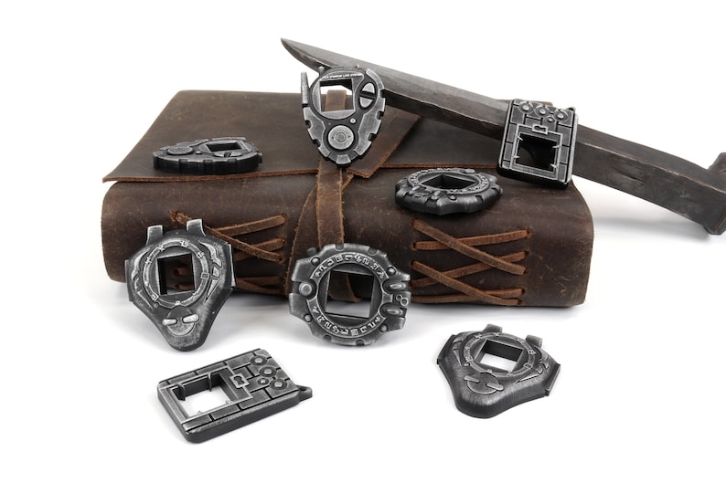 May include: Eight silver-colored metal charms shaped like digital watches with different designs. The charms are arranged on a brown leather-bound journal with a silver knife.