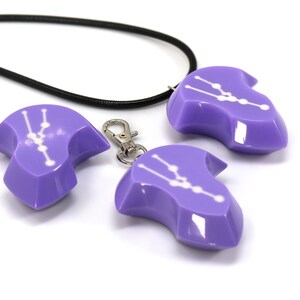 May include: Three purple pendants with a white constellation design. The pendants are shaped like a teardrop and have a shiny finish. One pendant is attached to a black cord necklace, while another is attached to a silver key chain.