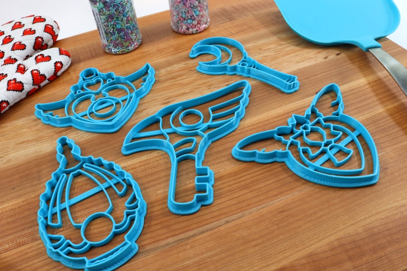 May include: Five blue plastic cookie cutters shaped like different magical wands and staffs. The cutters are on a wooden surface.