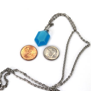 May include: A silver chain necklace with a light blue, faceted, hexagonal pendant. The pendant is about the size of a US penny.