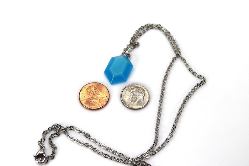 May include: A silver chain necklace with a light blue, faceted, hexagonal pendant. The pendant is about the size of a US penny.