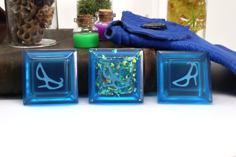 May include: Three blue square tiles with a white design of a high heel shoe on each. The middle tile has a glittery blue background.