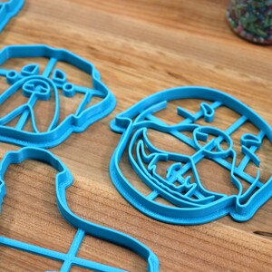 May include: A set of blue plastic cookie cutters shaped like a dog's face. The cutters are on a wooden surface.