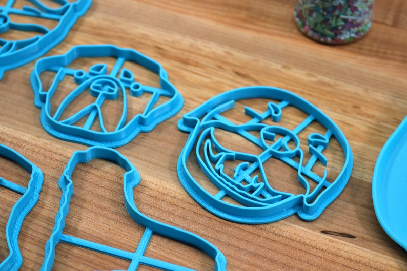 May include: A set of blue plastic cookie cutters shaped like a dog's face. The cutters are on a wooden surface.