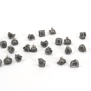 May include: A set of 18 grey earrings with different symbols and designs. The earrings are made of a metal alloy and have a silver finish.
