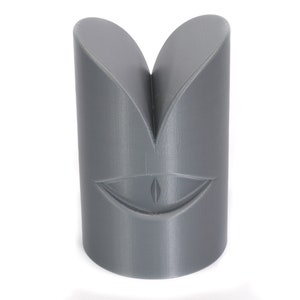 May include: Grey 3D printed object shaped like a face with a single eye and a wide smile.