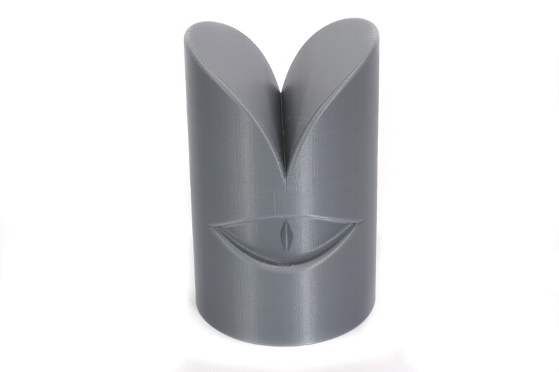 May include: Grey 3D printed object shaped like a face with a single eye and a wide smile.
