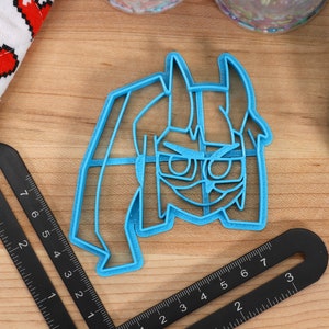 May include: A blue plastic cookie cutter shaped like a cartoon character with glasses and horns. The character has a serious expression.