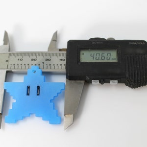 May include: A blue plastic star-shaped charm with a hole at the top, measured with a digital caliper to be 40.60 mm wide.