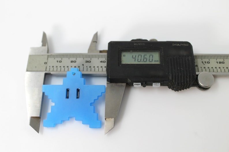 May include: A blue plastic star-shaped charm with a hole at the top, measured with a digital caliper to be 40.60 mm wide.
