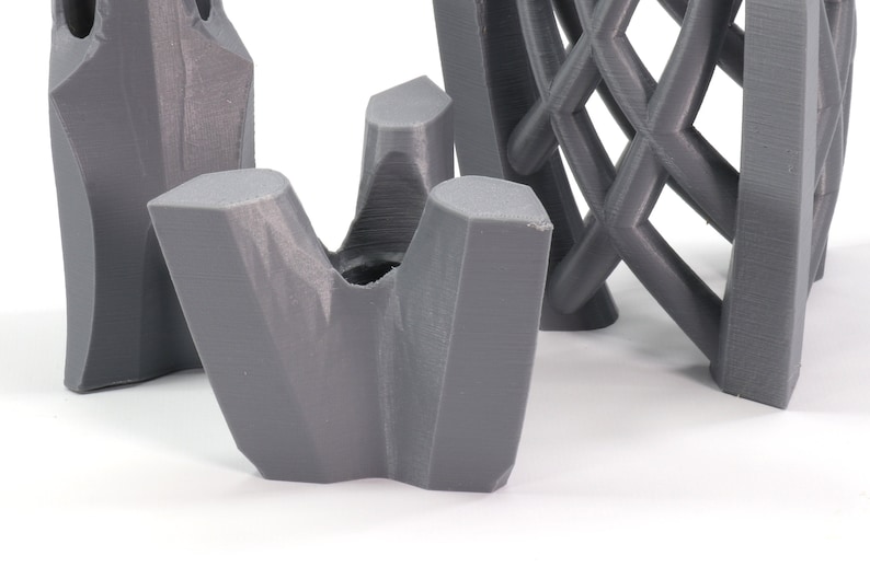 May include: Three gray 3D printed objects. The first object is a tall, narrow, rectangular shape with a textured surface. The second object is a short, wide, rectangular shape with a textured surface. The third object is a small, three-pronged object with a textured surface.
