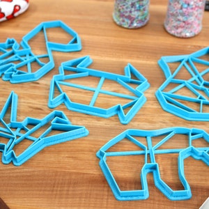 May include: Five blue plastic cookie cutters shaped like origami animals. The cutters are on a wooden surface.